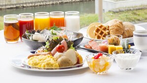 A breakfast table with various dishes and drinks, a view of a brick building, and a canal in the background. - Hotel Nord Otaru (Otaru)