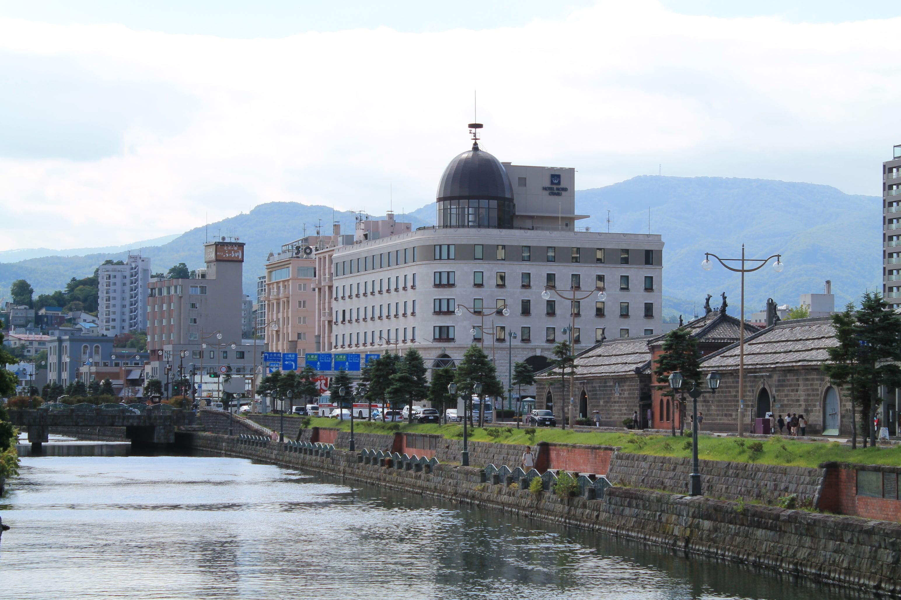 Un río con un puente de piedra, un edificio grande con una cúpula y montañas al fondo.