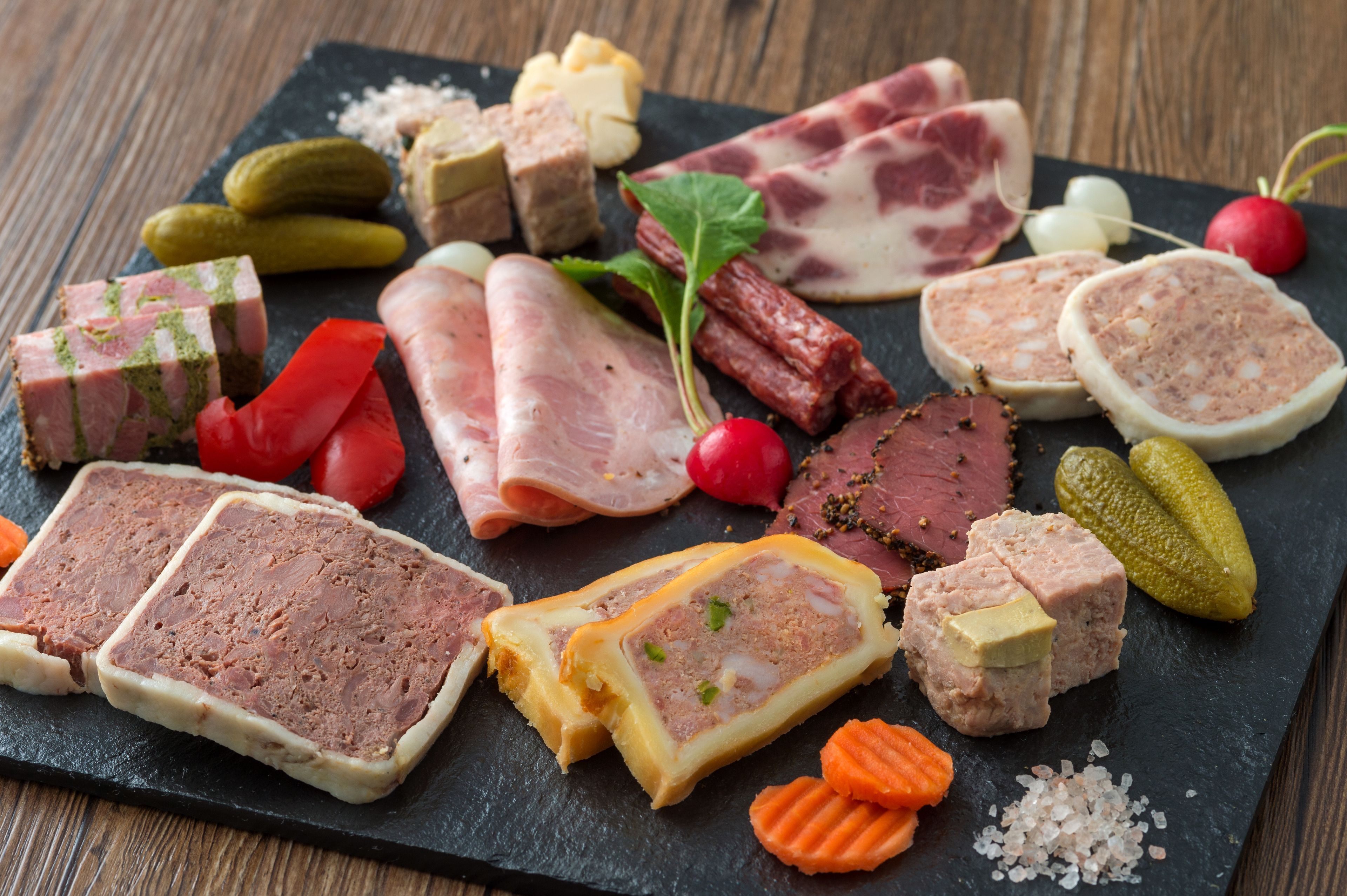 A variety of meats and pickles on a slate board.