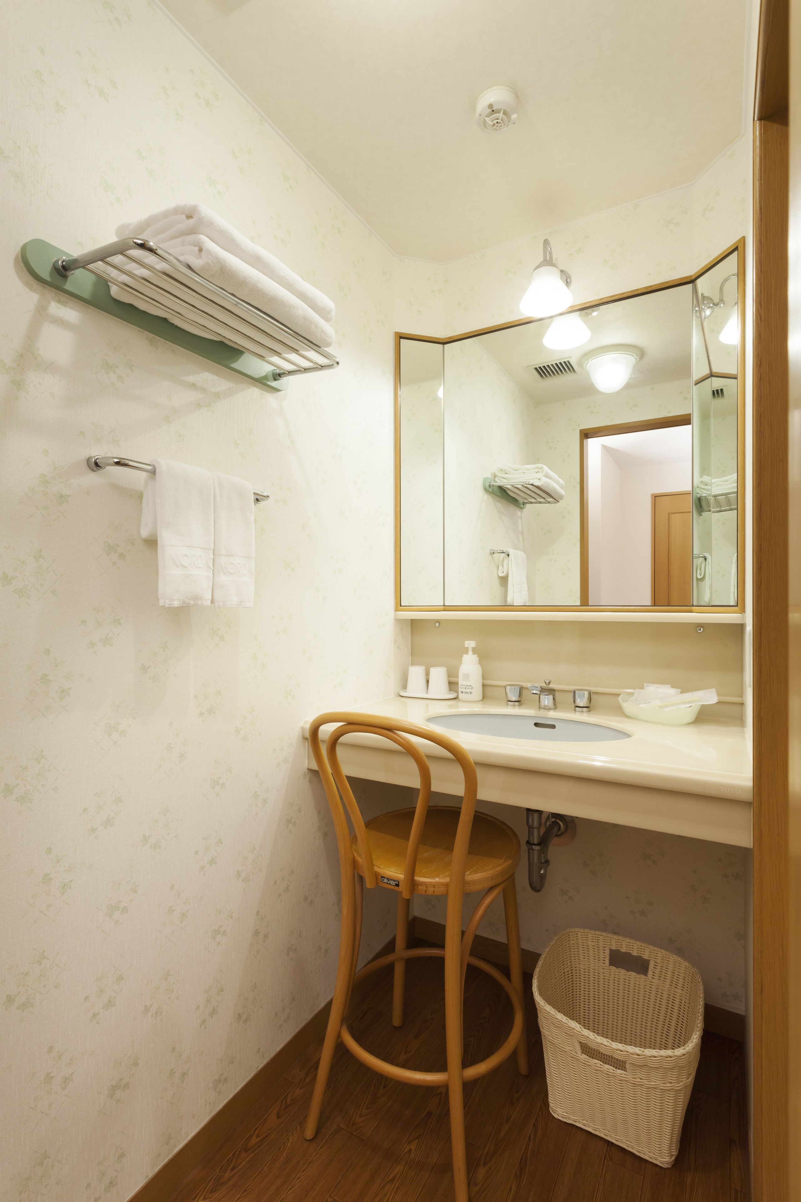 Un baño con una silla de madera, un lavamanos, un espejo y un perchero para toallas.