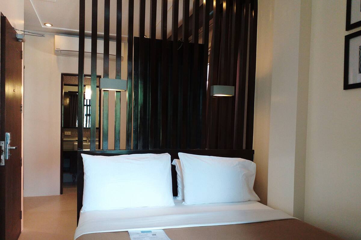 A hotel room with a bed, a door, a mirror, and a window with curtains.