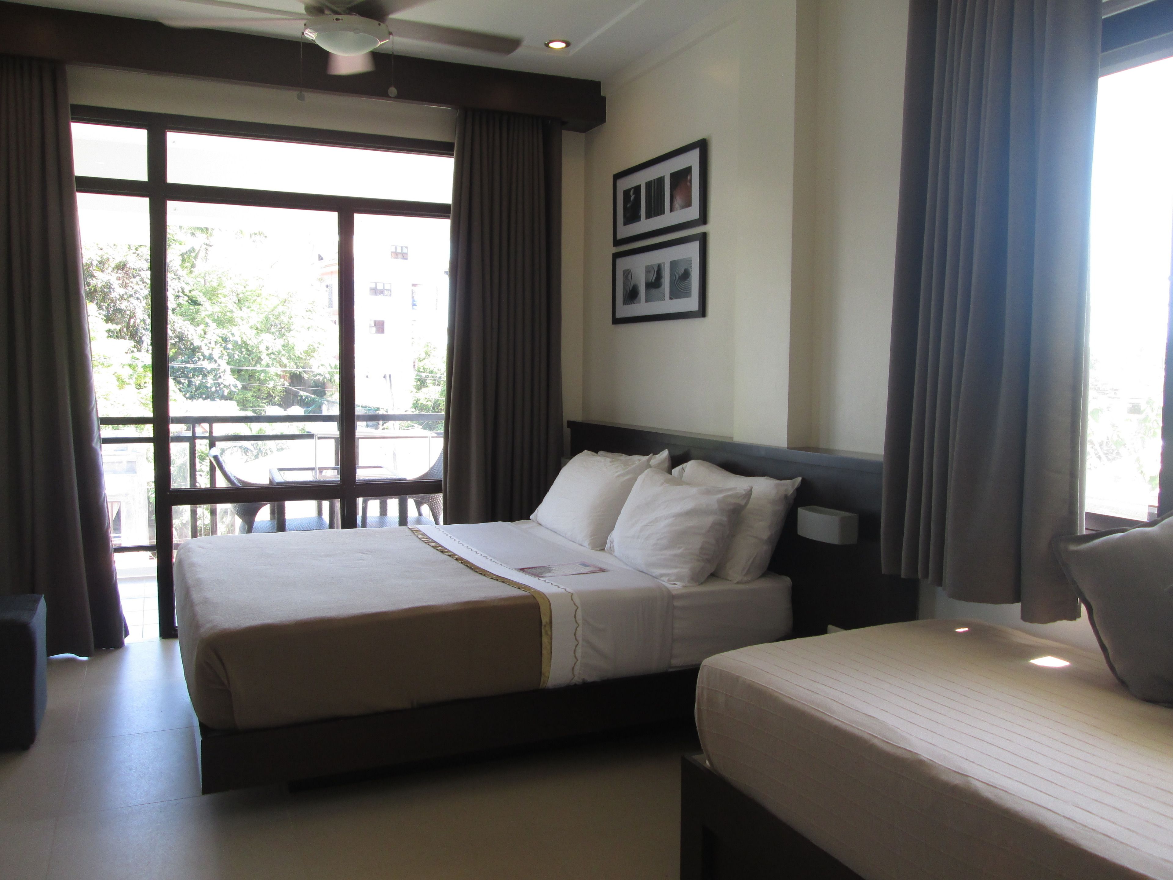 A hotel room with two beds, a balcony, and large windows.