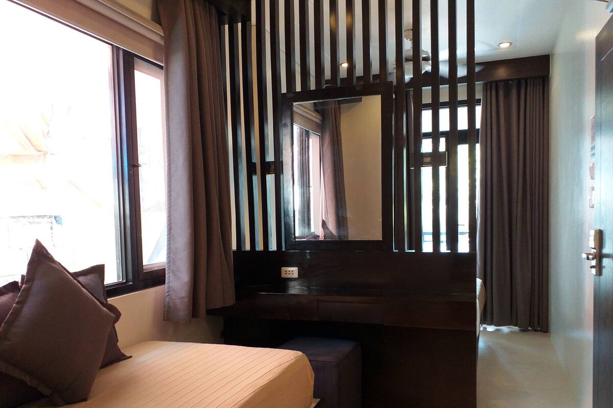 A hotel room with a bed, a desk, a mirror, and a door.