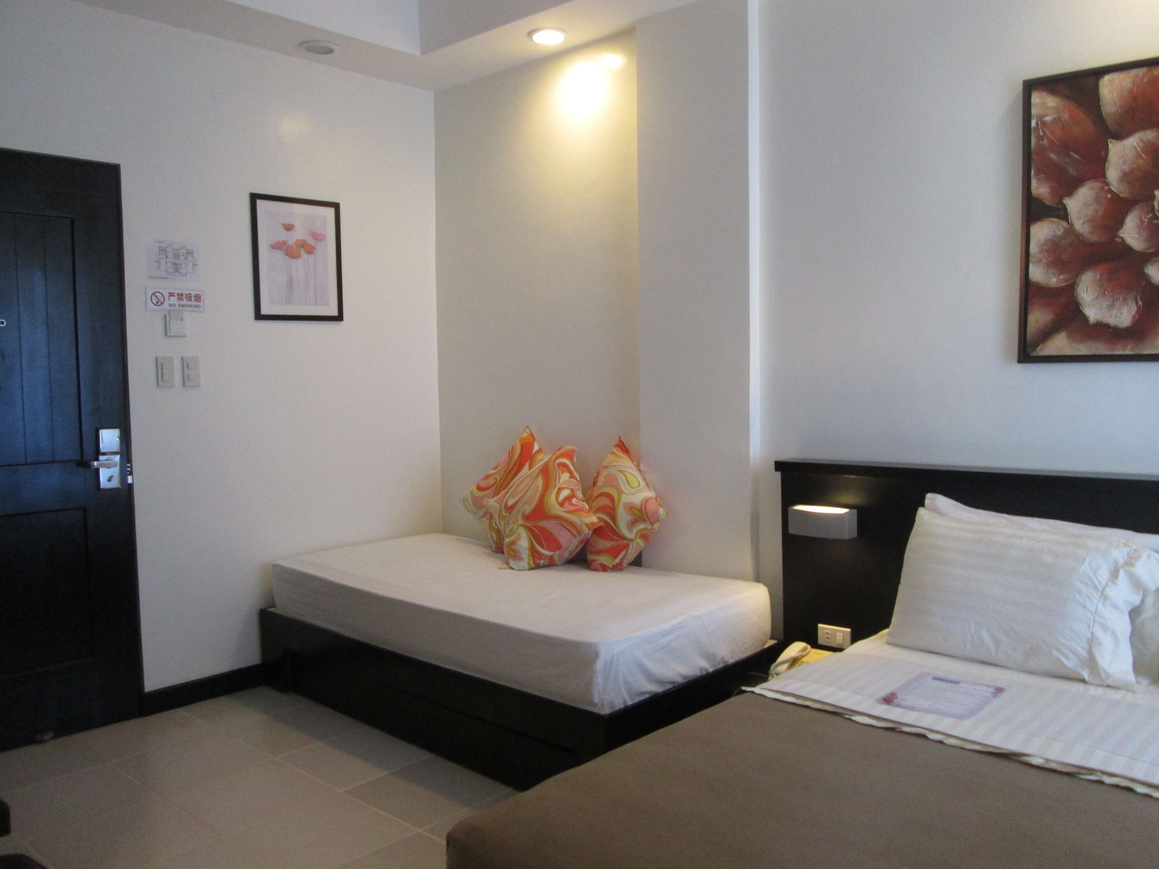 Una habitación de hotel con cama, una zona de estar pequeña, una puerta y una lámpara fijada a la pared.