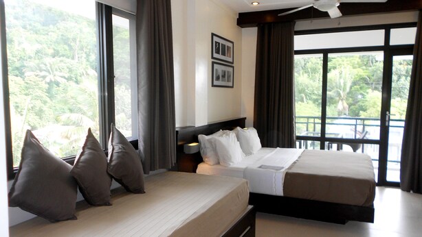 Habitación de hotel con dos camas, ventanas amplias, ventilador de techo y vistas a zonas verdes.