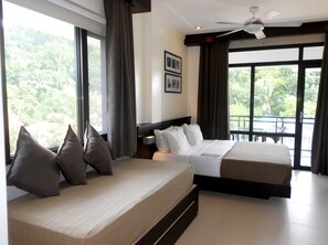 A hotel room with two beds, large windows, a ceiling fan, and a view of greenery outside. - One Crescent Place (Boracay Island)
