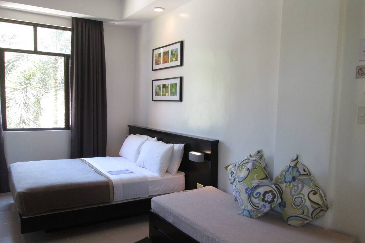 A hotel room with two beds, a window with curtains, and two framed pictures on the wall.
