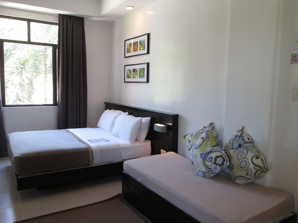 A hotel room with two beds, a window with curtains, and two framed pictures on the wall. - One Crescent Place (Boracay Island)