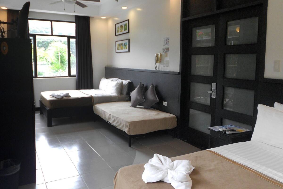 A hotel room with two beds, a ceiling fan, a window with curtains, and a door with glass panels.
