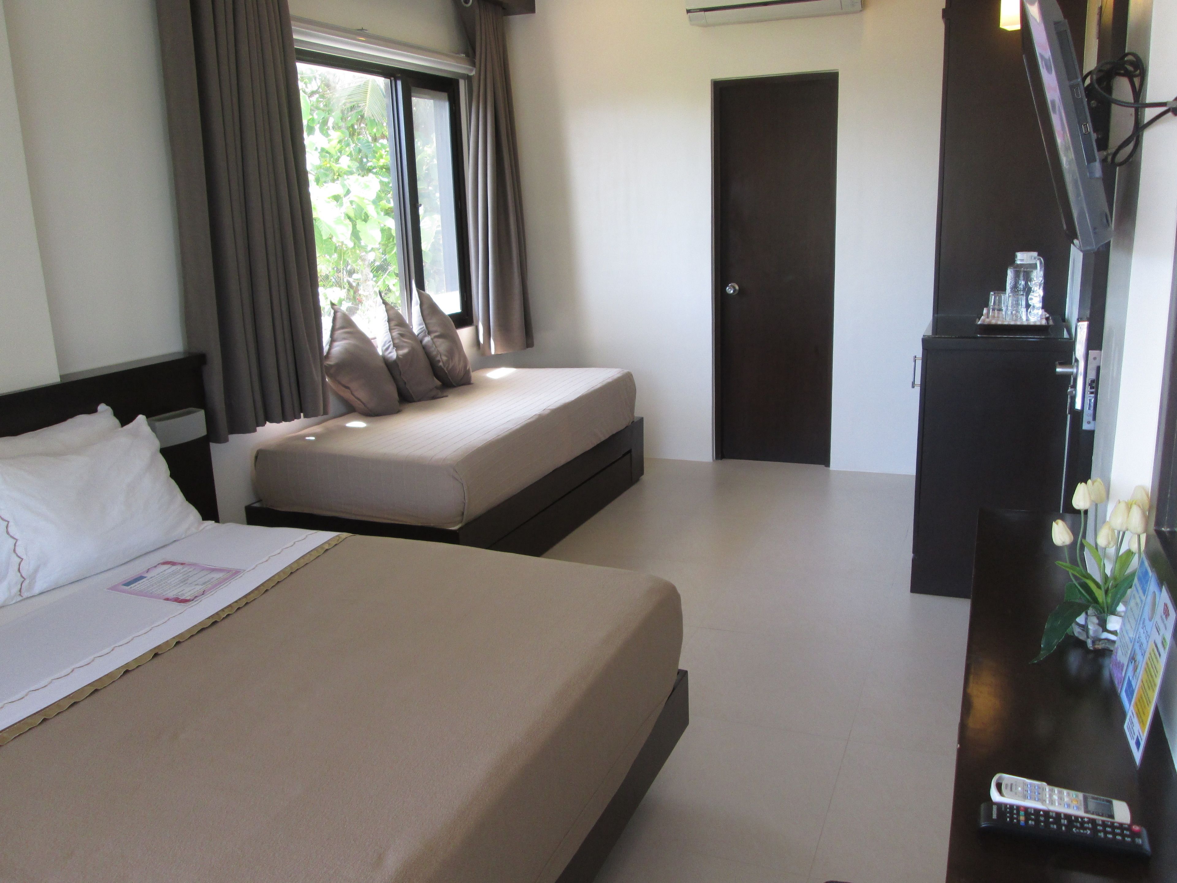 Una habitación de hotel con una cama grande, una cama más pequeña, un escritorio con una computadora y una ventana con cortinas.