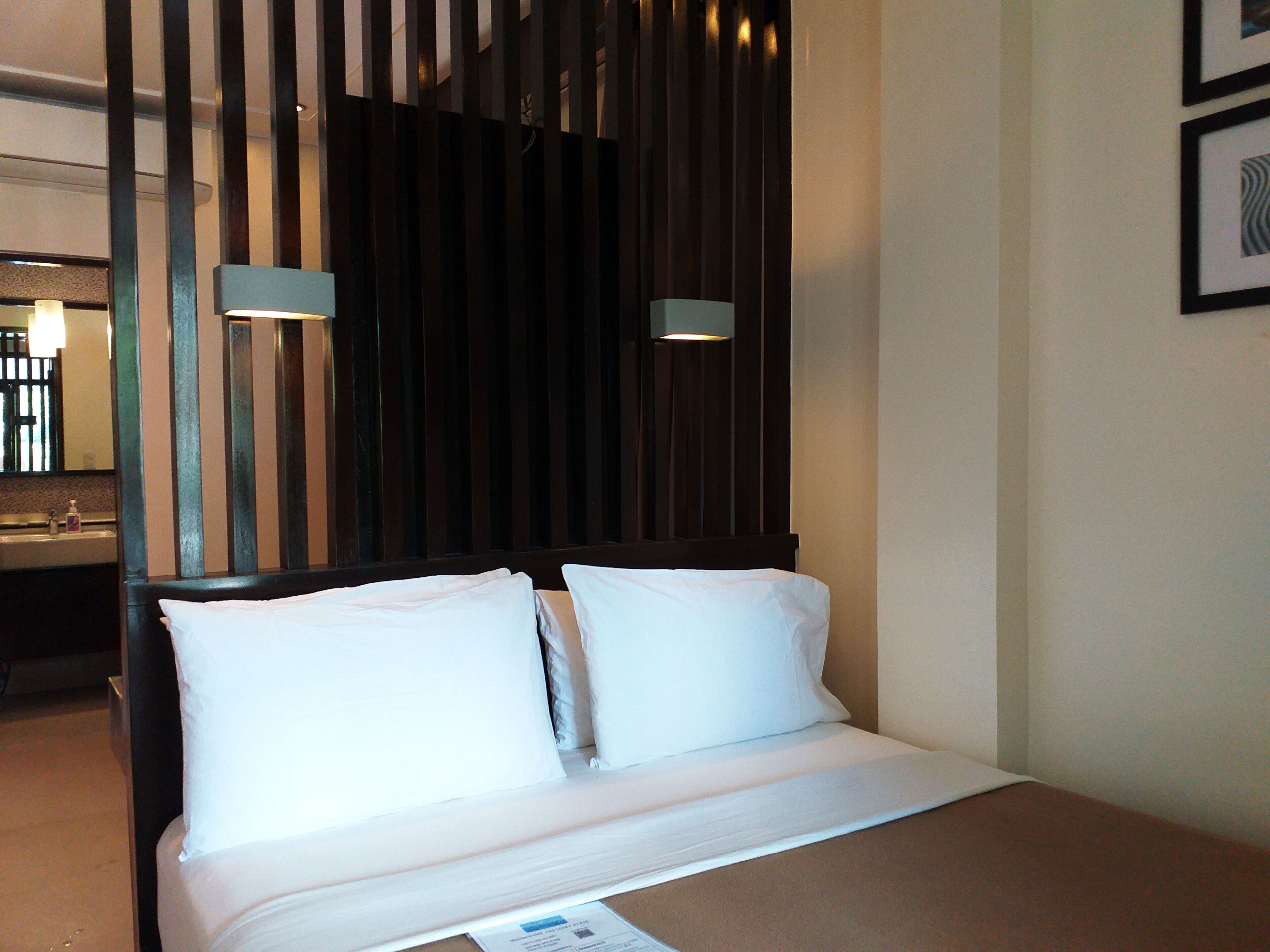 A hotel room with a bed, a nightstand, a mirror, and a wooden partition.