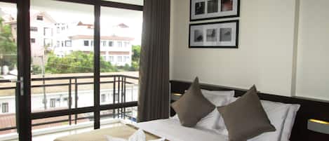 Una habitación de hotel con un ventanal grande, una cama con sábanas blancas y dos almohadas, una cortina y dos cuadros en la pared.