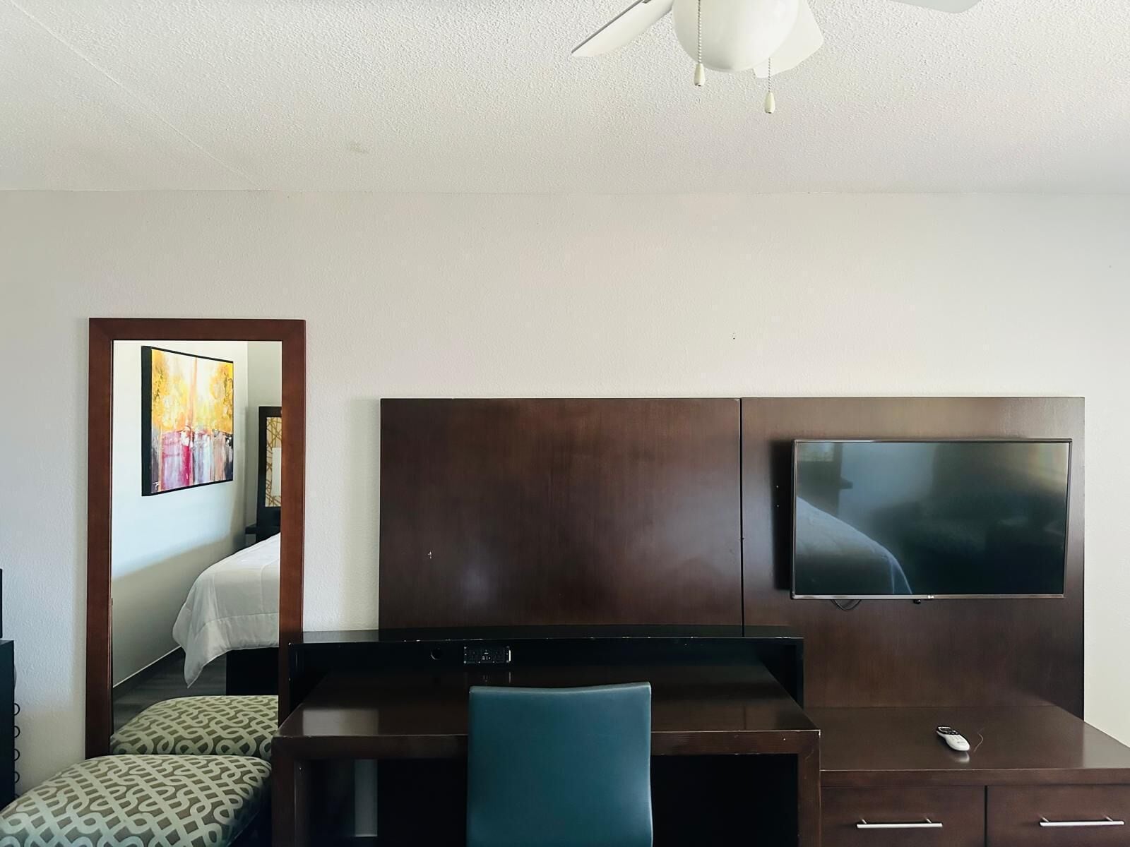 A hotel room with a bed, a desk, a chair, a TV, and a ceiling fan.
