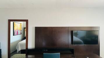 A hotel room with a bed, a desk, a chair, a TV, and a ceiling fan.