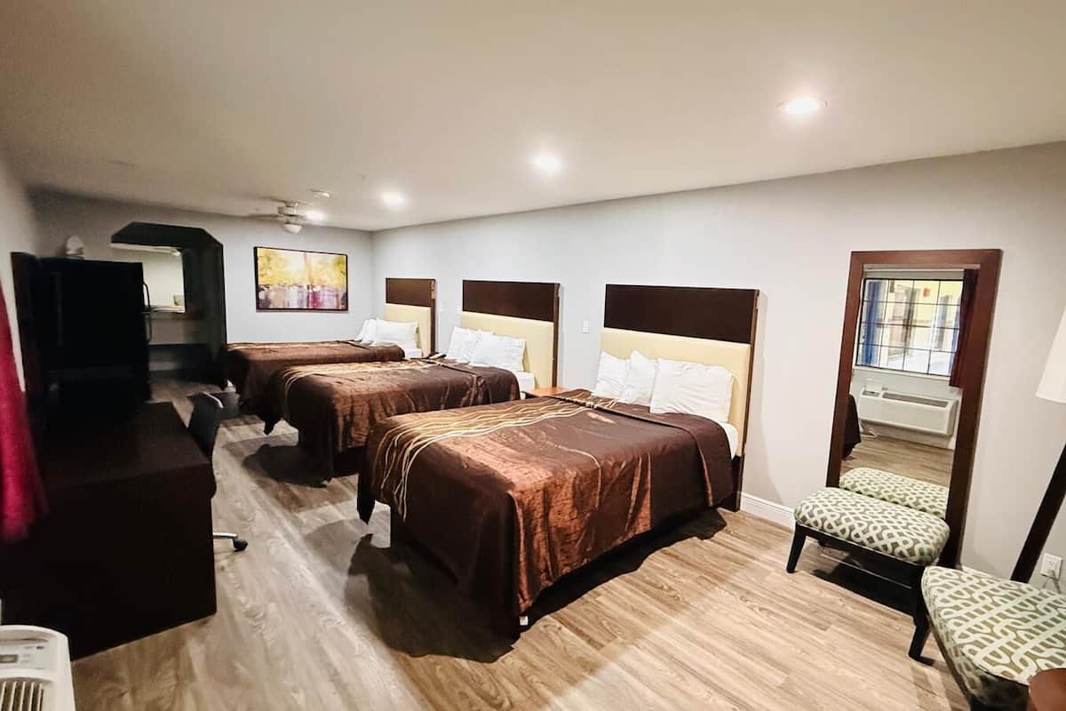 Ein Hotelzimmer mit drei Betten, einem Schreibtisch, einem Stuhl, einer Lampe und einem großen Spiegel.