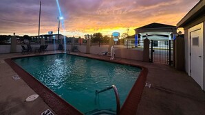 A swimming pool with a view of a sunset, a covered seating area, and a gated entrance. - The Executive Inn & Suites (West Columbia)