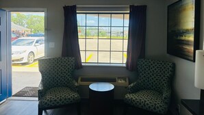 A room with two patterned chairs, a small table, a window with curtains, an air conditioning unit, and a painting on the wall. - The Executive Inn & Suites (West Columbia)
