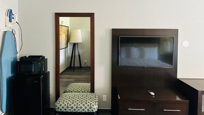 A hotel room with a TV, a desk with a computer, a lamp, and a mirror. - The Executive Inn & Suites (West Columbia)