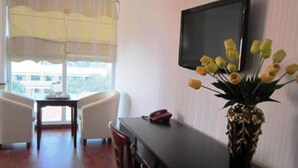 Une chambre d’hôtel avec un lit, un bureau, une chaise, une télévision et un vase avec des fleurs.