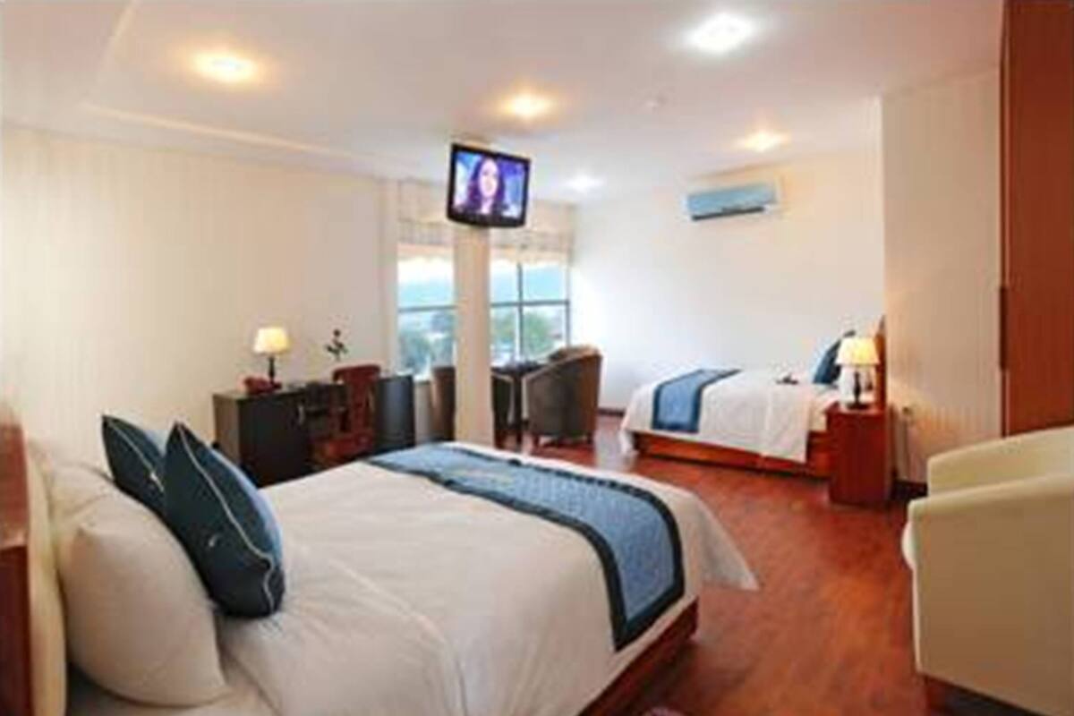 A hotel room with a large bed, a smaller bed, a desk, a chair, a TV, and a window.