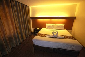 A hotel room with a bed, curtains, a nightstand, and a wall-mounted light. - The Ritz Hotel at Garden Oases (Davao)