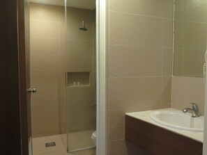 A bathroom with a glass-enclosed shower, a sink with a mirror, and beige tiles. - The Ritz Hotel at Garden Oases (Davao)