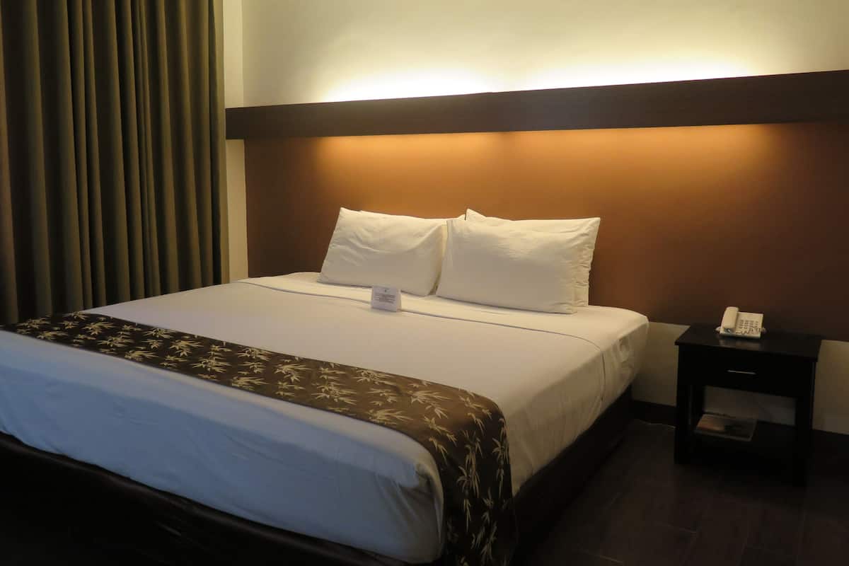A hotel room with a large bed, a nightstand with a phone, and a curtain.