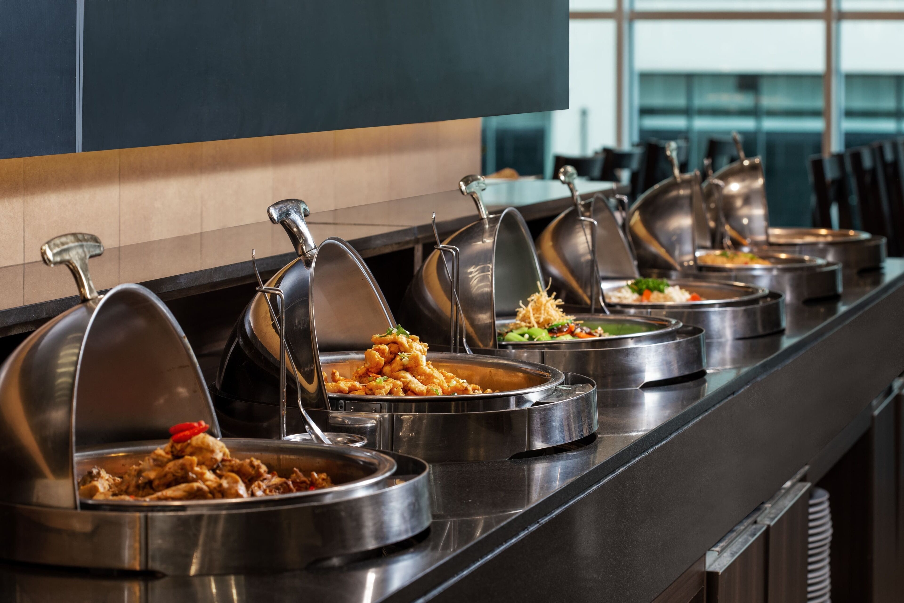 Una barra de buffet con diferentes platos en recipientes de metal.