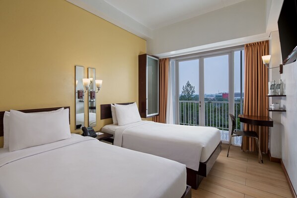 A hotel room with two beds, a desk, a chair, a TV, and a balcony with curtains.