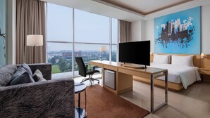 A hotel room with a large window, a desk with a flat-screen TV, a bed, and a painting on the wall. - Hotel Santika BSD City Serpong (South Tangerang)