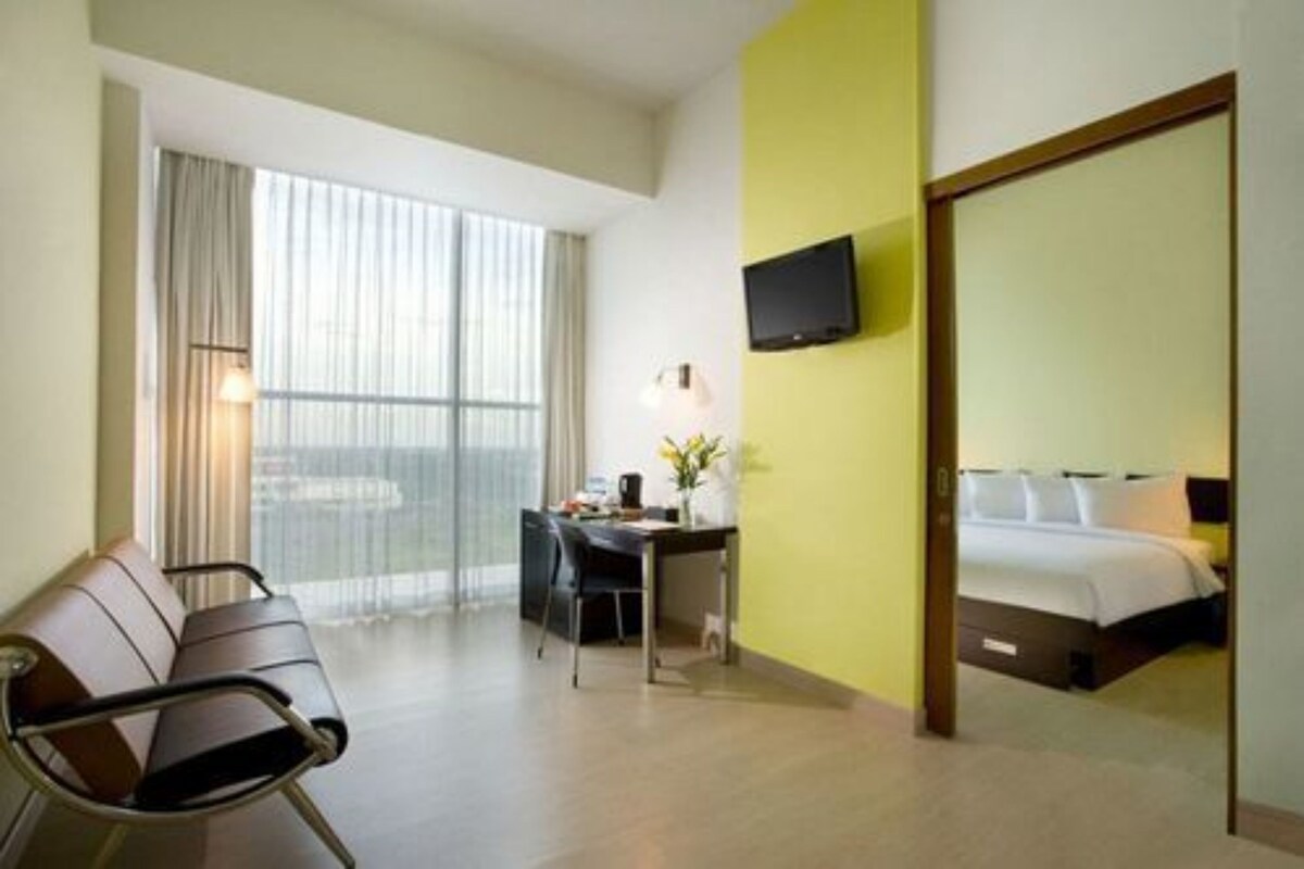 A hotel room with a bed, a desk with a chair, a television on the wall, and a window with curtains.