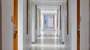 A long, narrow hallway with doors on both sides, leading to a room with a blue window at the end. - Hotel Santika BSD City Serpong (South Tangerang)