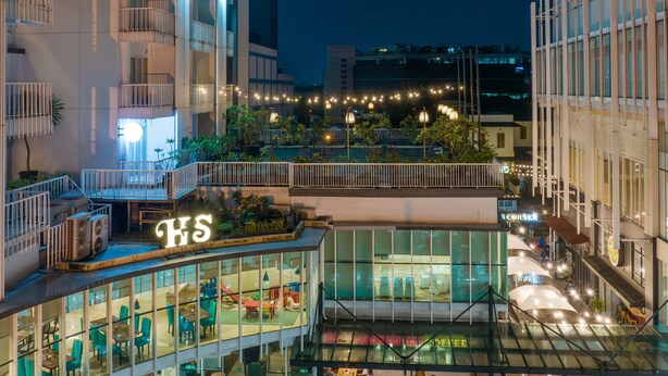 A hotel with a glass facade, outdoor seating area, and a sign with 'HS' illuminated. - Hotel Santika BSD City Serpong (South Tangerang)
