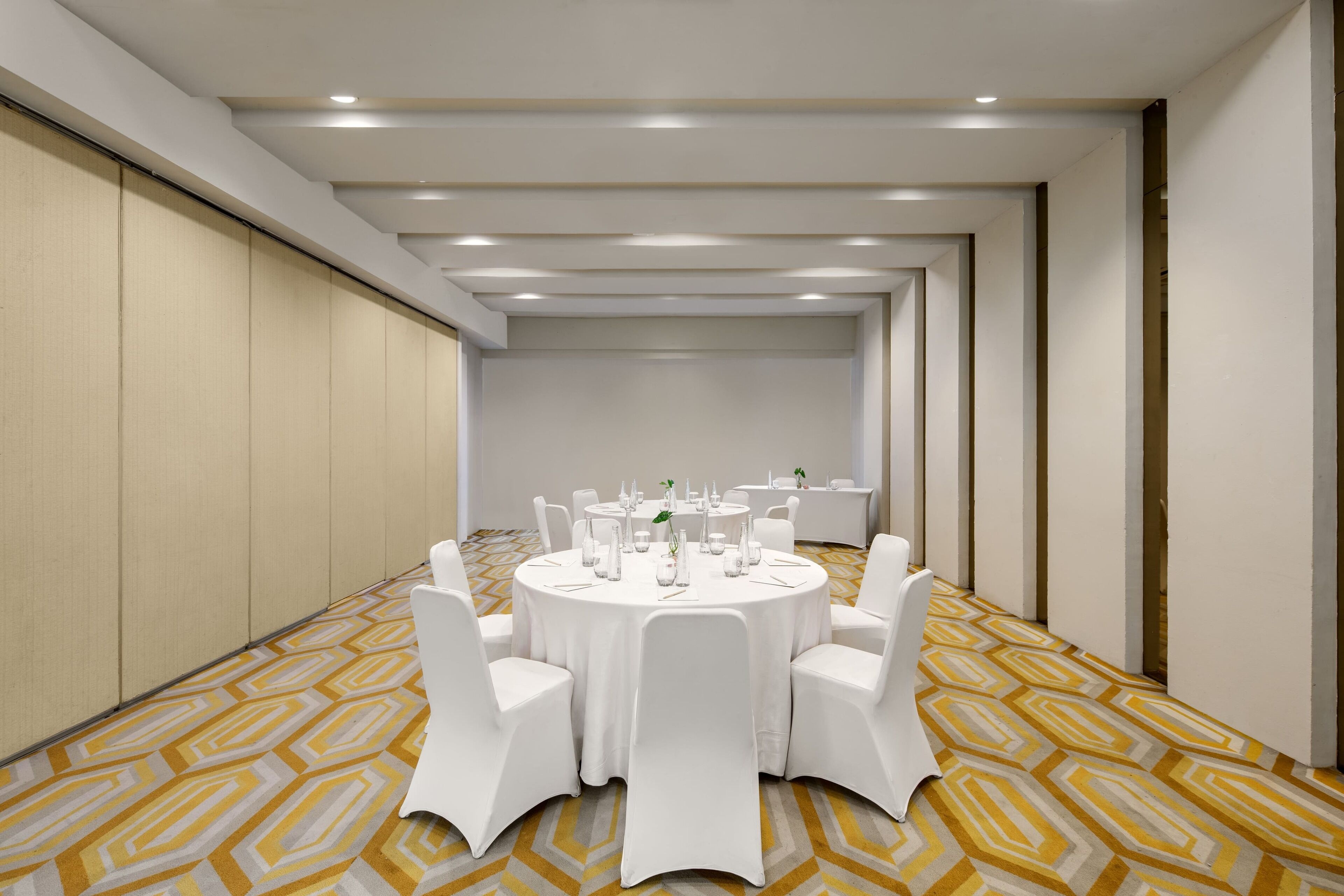 A conference room with round tables, white chairs, and a patterned carpet.
