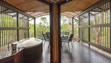 A wooden deck with a hot tub, outdoor seating, and a view of the surrounding greenery.