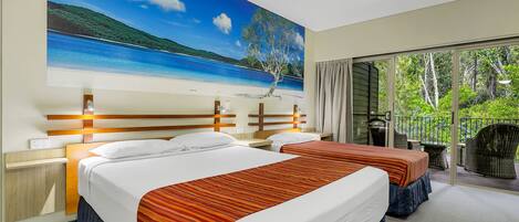 Habitación de hotel con dos camas, un gran mural de playa en la pared y un balcón con vistas a zonas verdes.