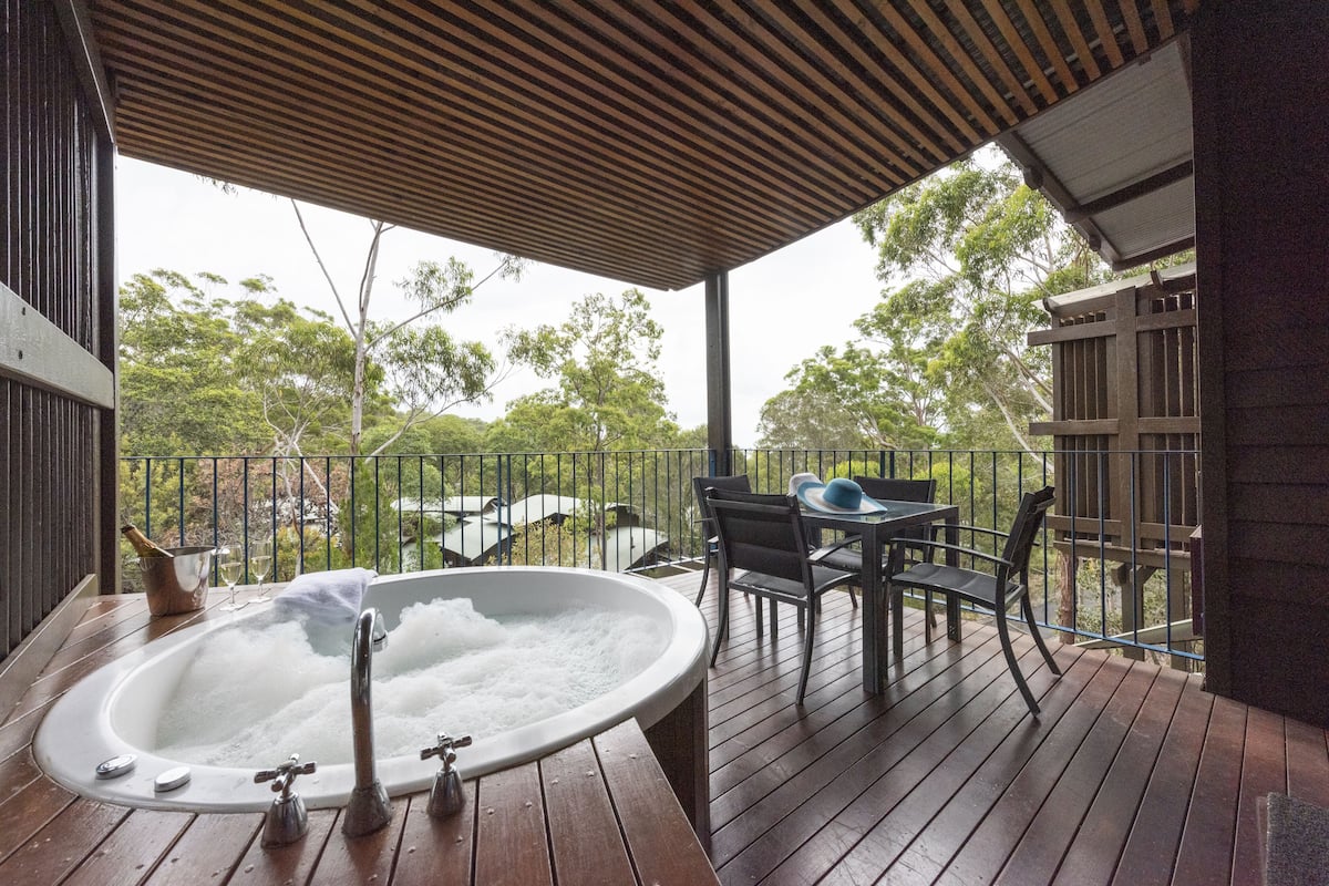 A wooden deck with a hot tub, outdoor seating, and a view of trees.