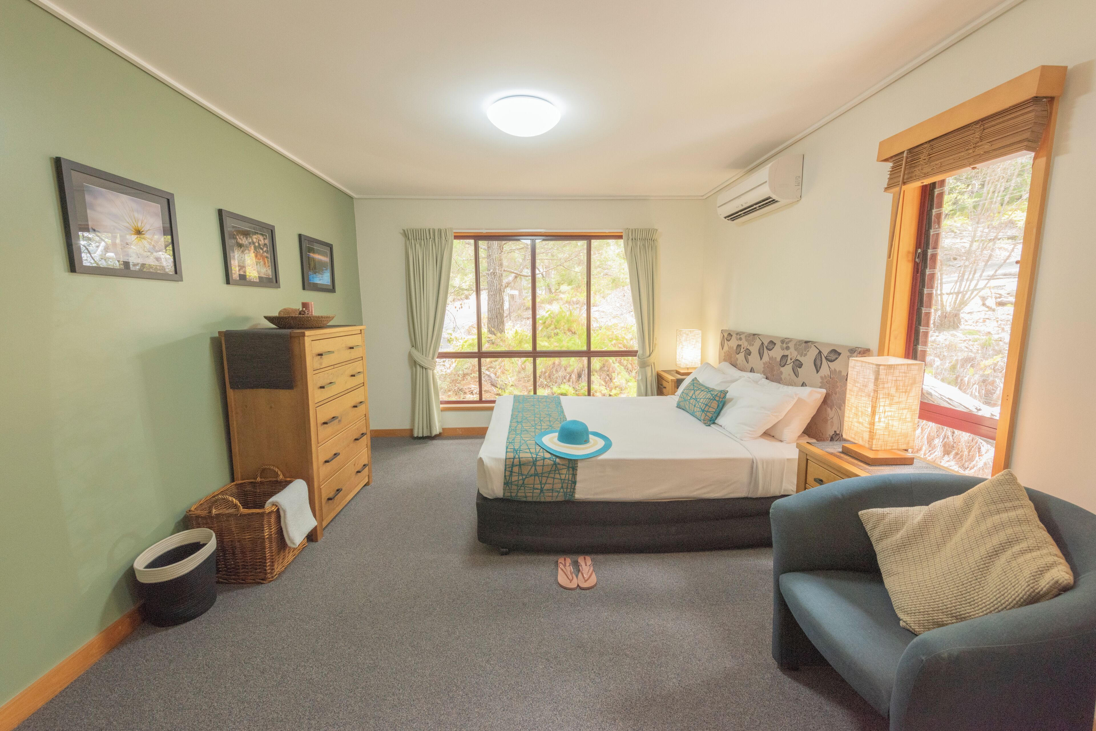 A bedroom with a bed, a nightstand, a dresser, a window with curtains, and a wall-mounted air conditioner.