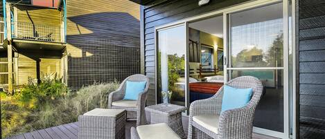 A deck with wicker furniture, a glass door leading to a room, and a balcony with a railing.