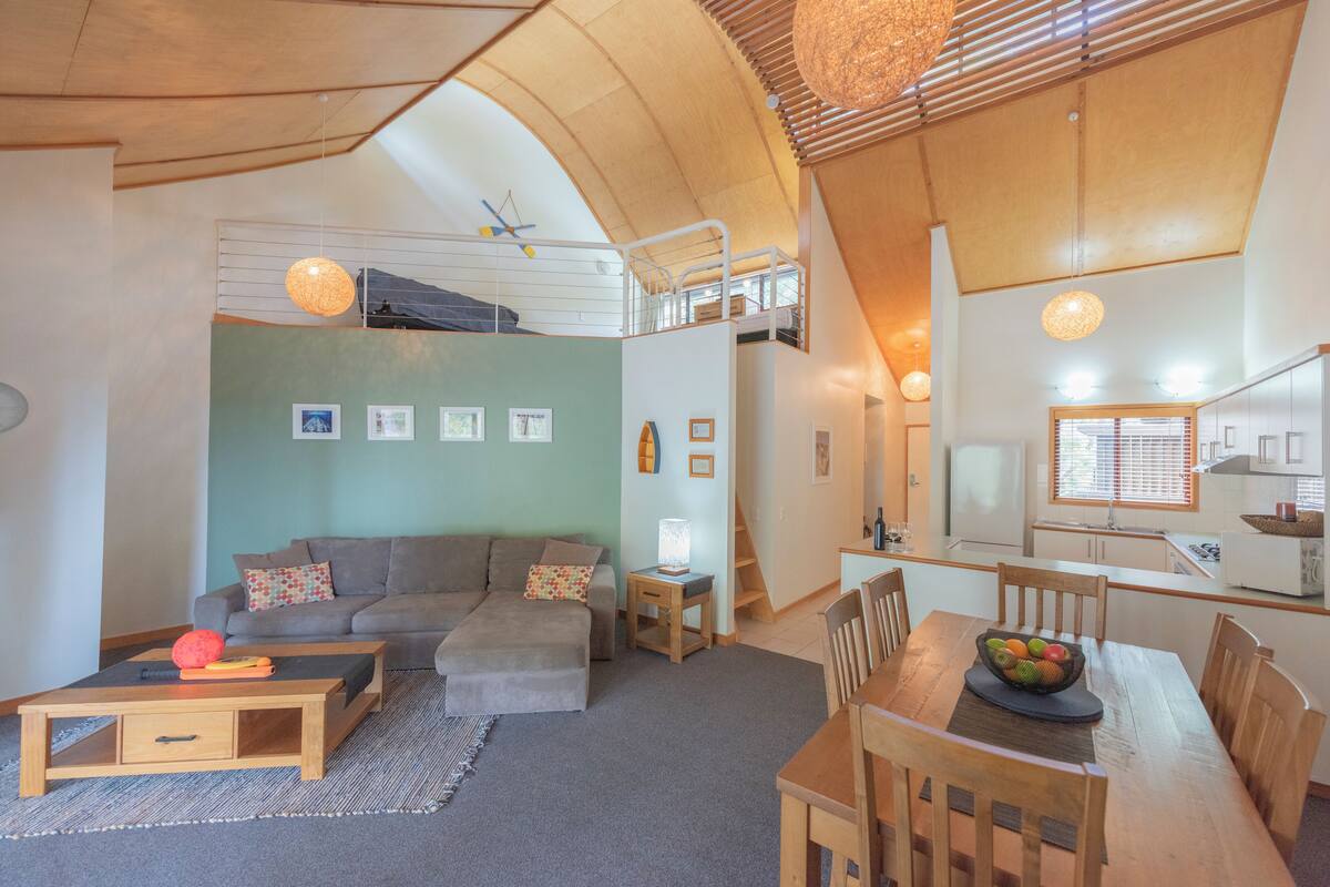 A spacious living area with a loft bedroom, a dining table with chairs, and a kitchen area.