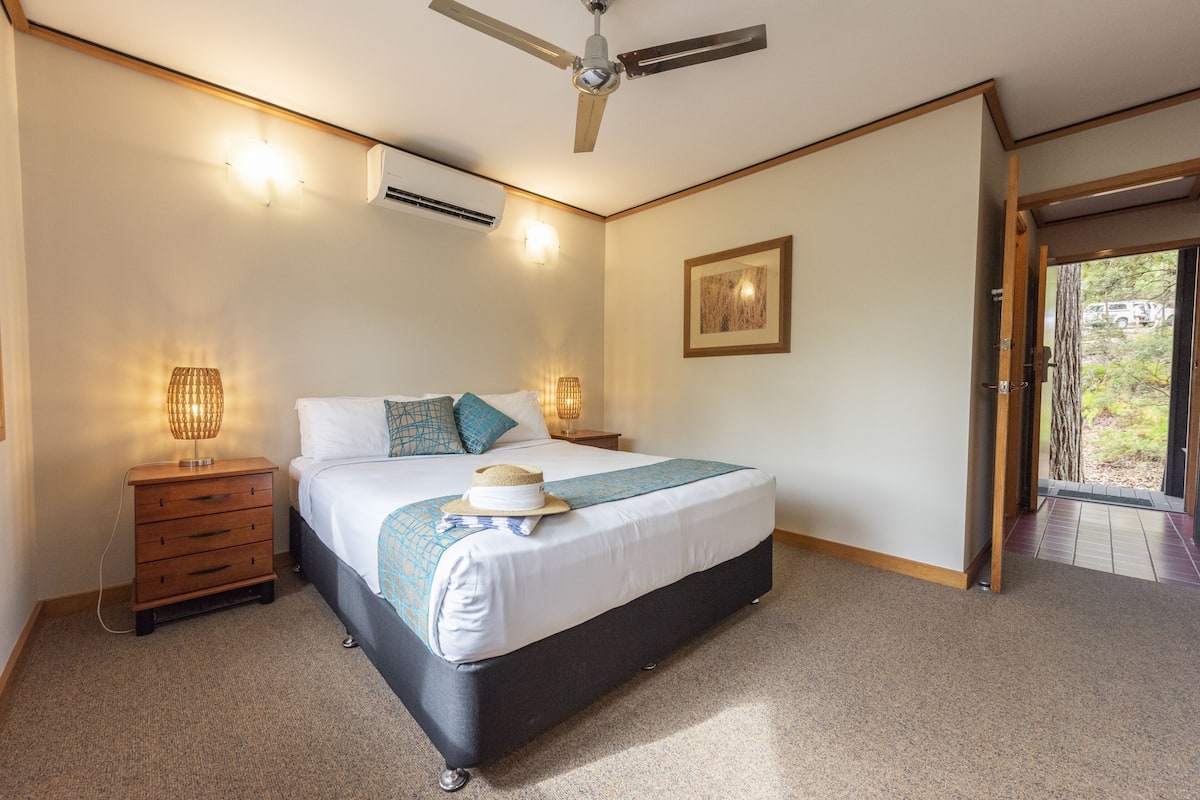 A bedroom with a bed, bedside tables, a ceiling fan, and a door leading to an outdoor area.