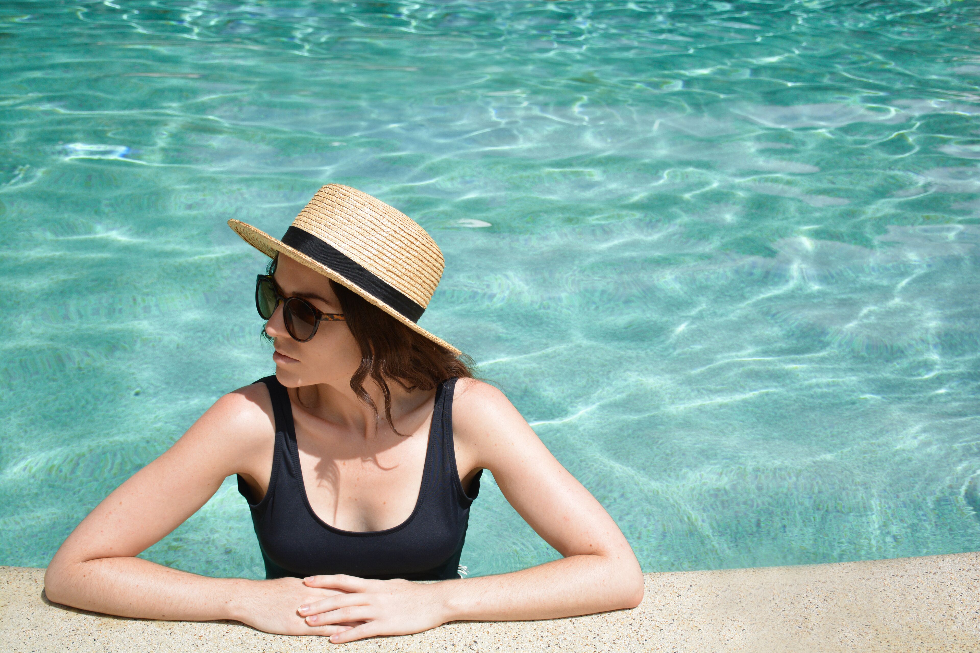 A person in a swimsuit and straw hat by a clear pool.