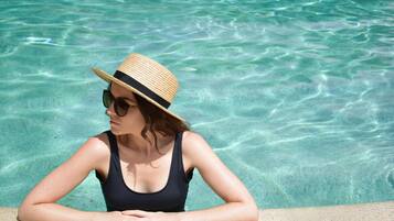 A person in a swimsuit and straw hat by a clear pool.