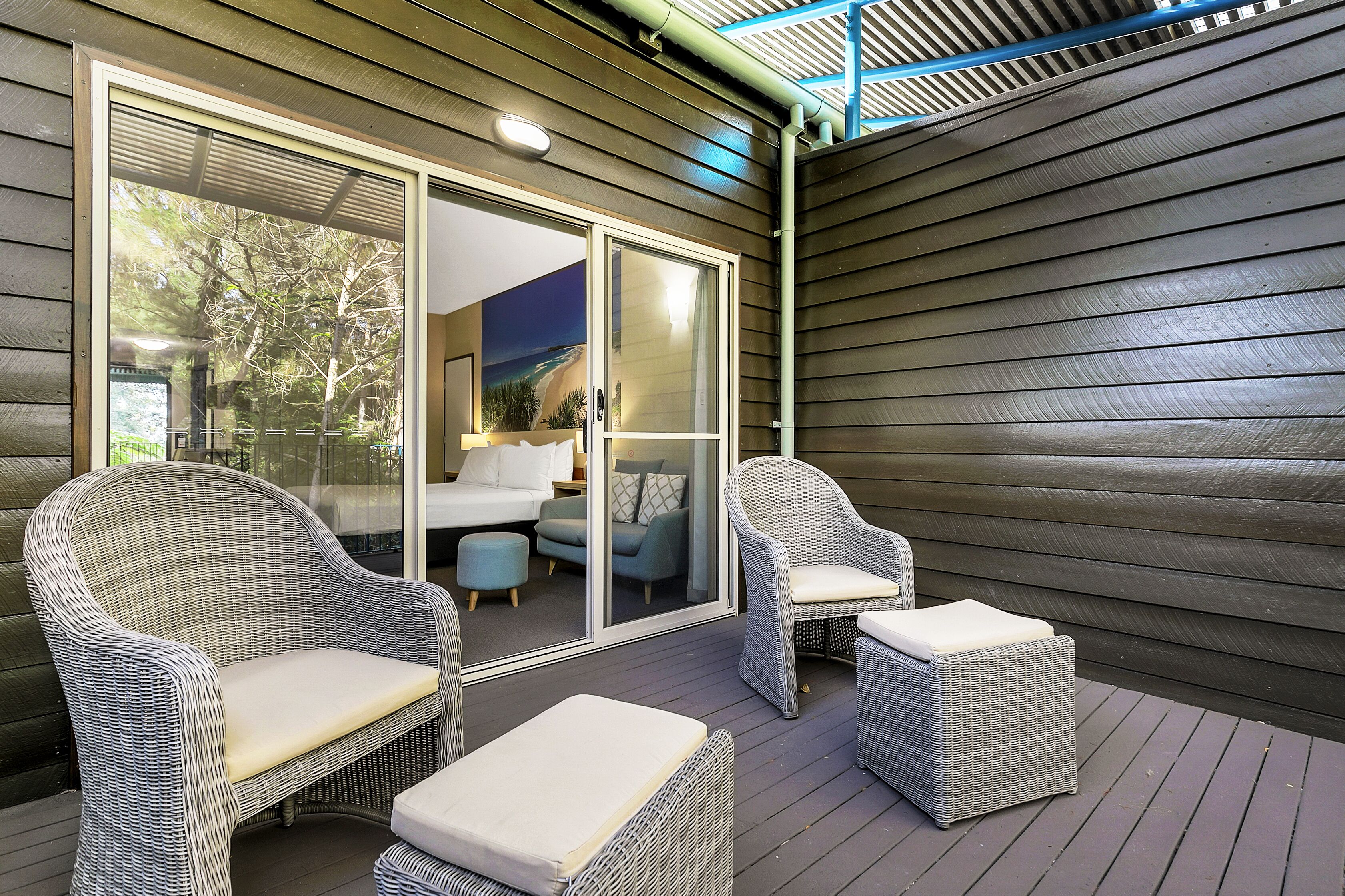 A covered outdoor seating area with wicker furniture and a sliding glass door leading to an interior space.