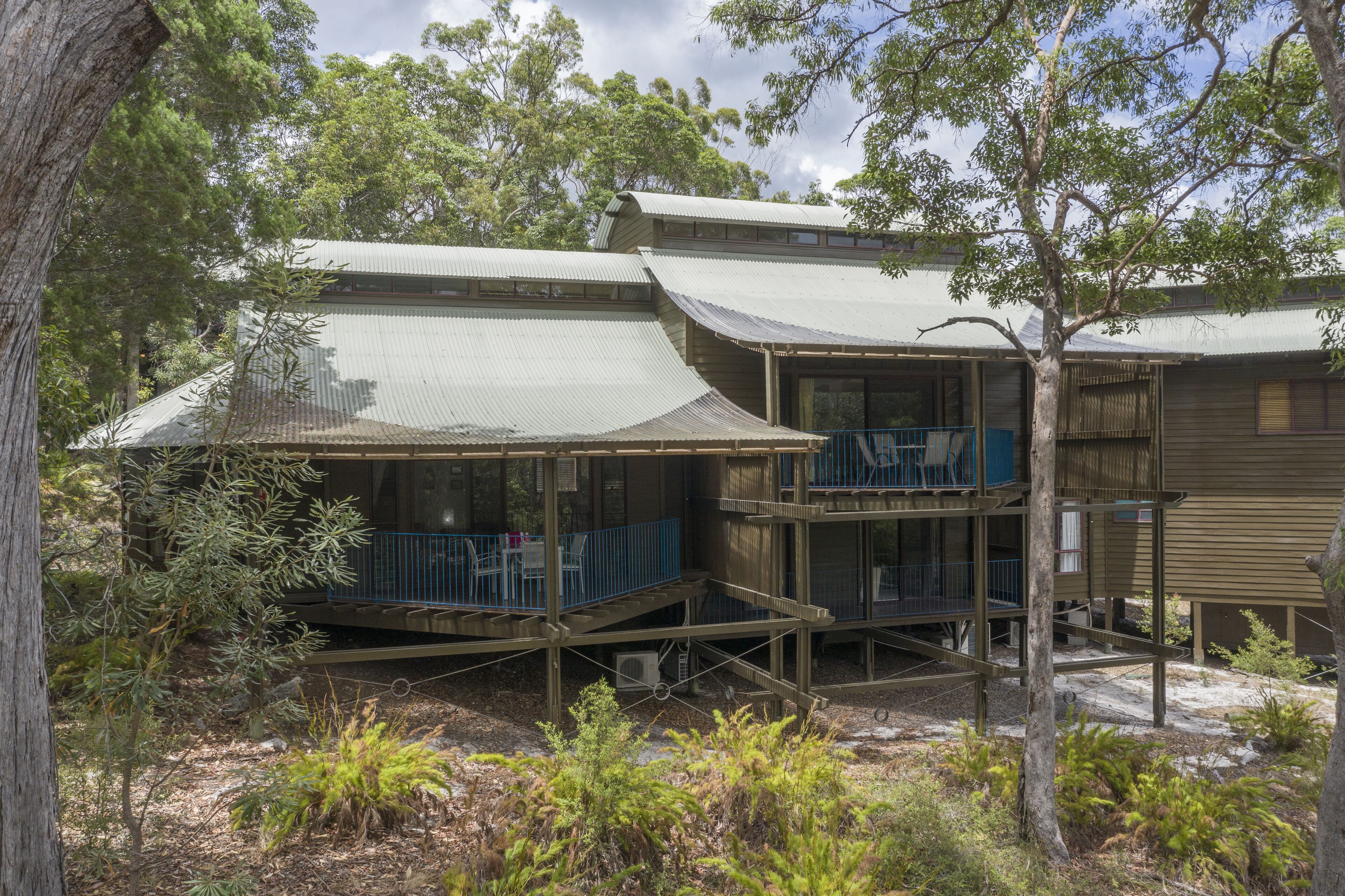 A two-story wooden building with a flat roof, surrounded by trees.