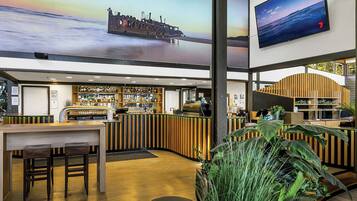 A bar area with a wooden counter, bar stools, and a large screen displaying a sunset over water.
