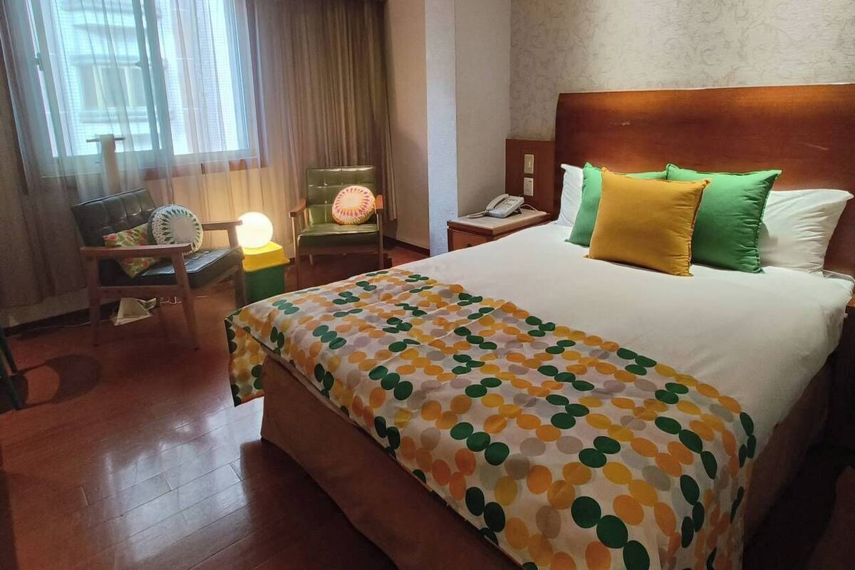 Ein Hotelzimmer mit einem großen Bett, einem Nachttisch aus Holz, einem Sessel, einem Schreibtisch und einer Lampe.
