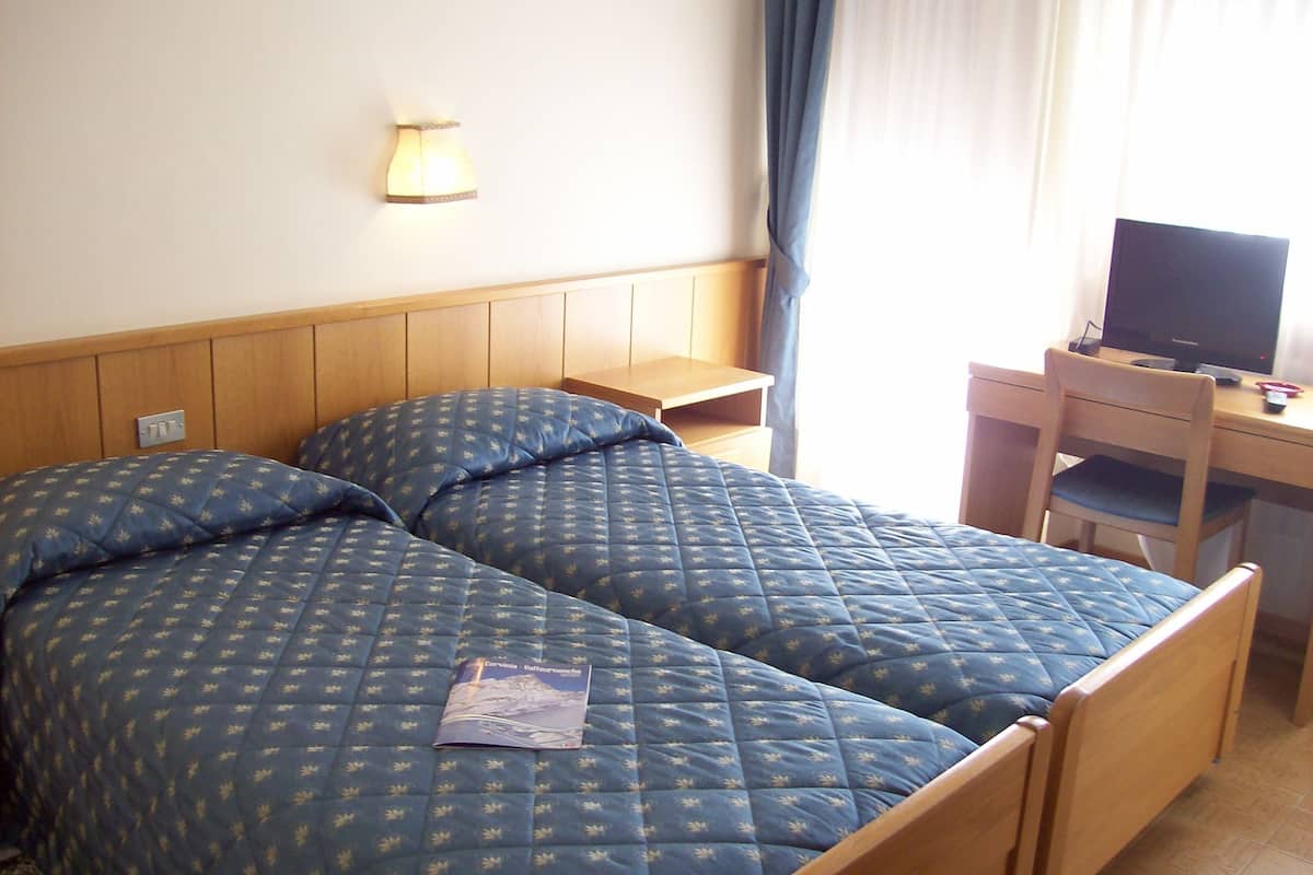 Een hotelkamer met twee bedden, een bureau met een computer en een lamp aan de muur.