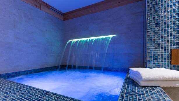 A hot tub with a waterfall feature, surrounded by tiled walls and wooden beams. - Punta Margherita (Valtournenche)