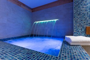 A hot tub with a waterfall feature, surrounded by tiled walls and wooden beams. - Punta Margherita (Valtournenche)